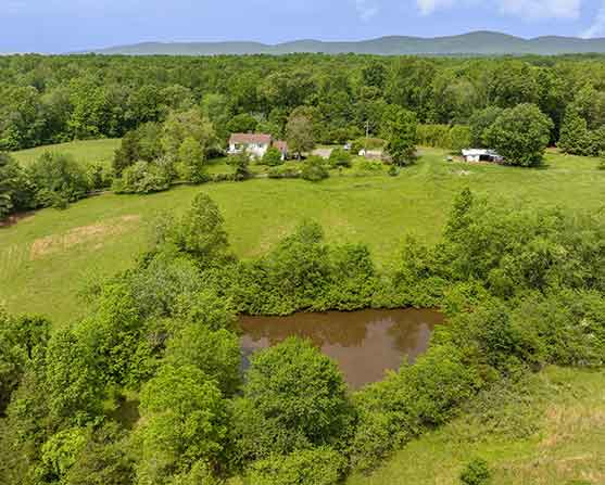 Aerial view of 66.52-acre farm in Orange, Virginia, with pond, pasture, renovated farmhouse, and mountain views at 1701 Harrington Road.