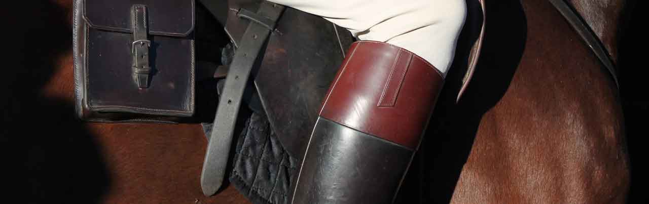 This image captures a close-up of an equestrian's leather riding boot and saddle, highlighting the craftsmanship and detail of the gear. The rich tones of the leather contrast with the horse's coat and the rider's light breeches, showcasing a classic and functional style for horseback riding.